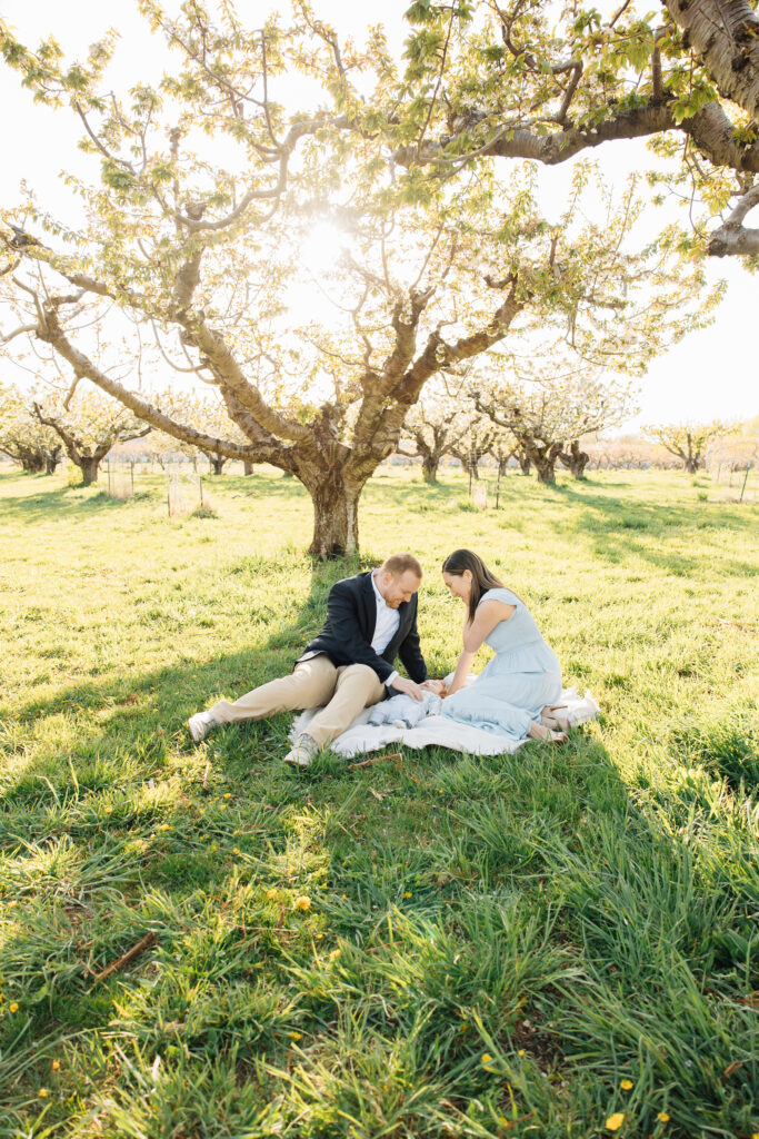 Mother and Father snuggle baby in spring mini session in orchard