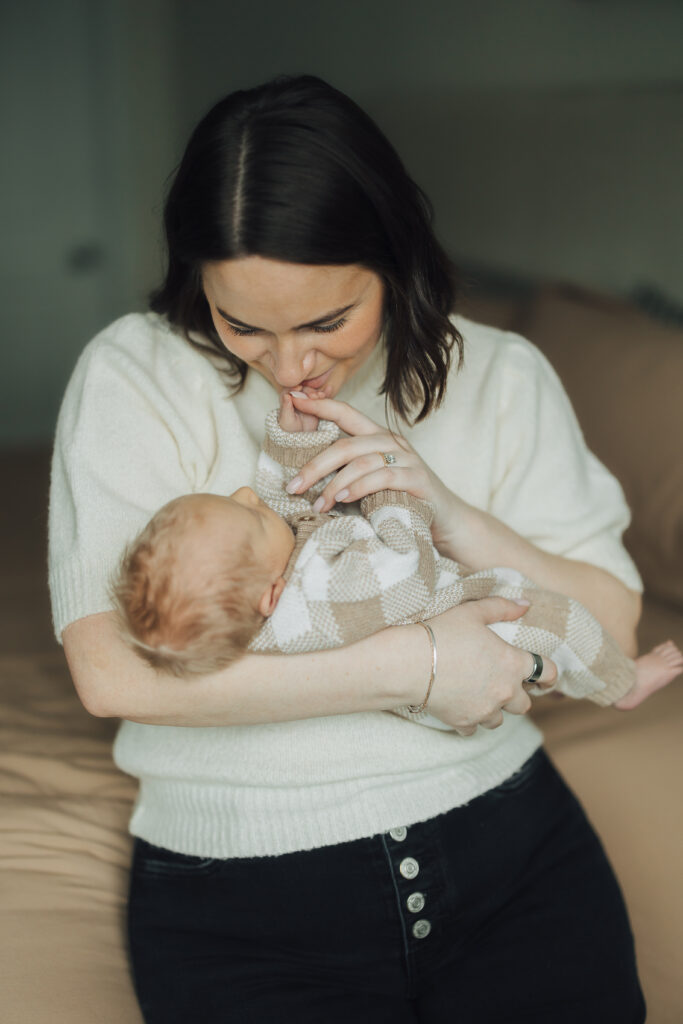 Mom kisses baby's hand in lifestyle newborn session in Saratoga Springs